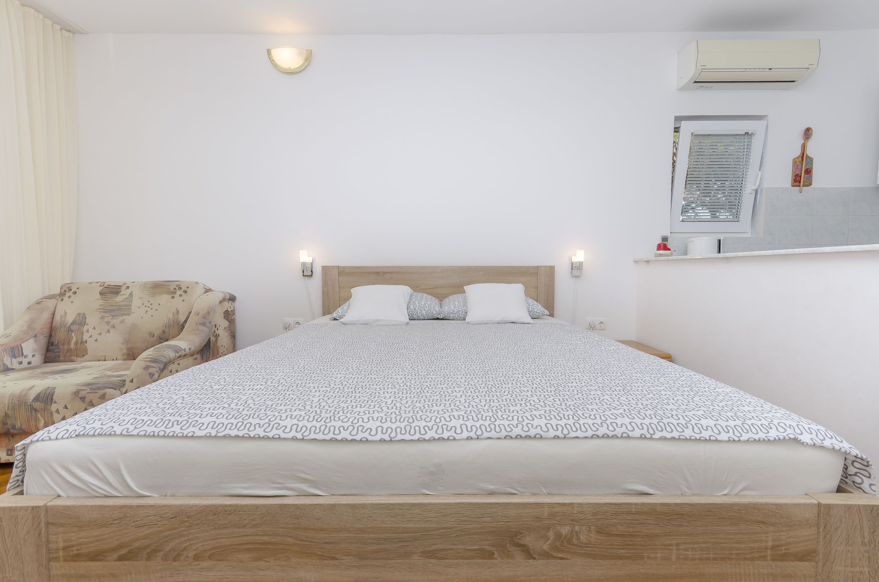 A neatly arranged bedroom with a bed, bedside lamps, a chair, and a small shelf with items.