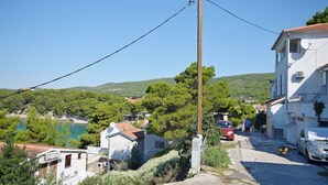 A coastal village with a narrow street, buildings with red-tiled roofs, and a clear view of the sea and hills in the background. - Apartments Vlasta (Tribunj)
