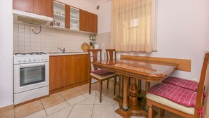A kitchen with wooden cabinets, a gas stove, and a dining table with chairs. - Apartment Mario (Rogoznica)