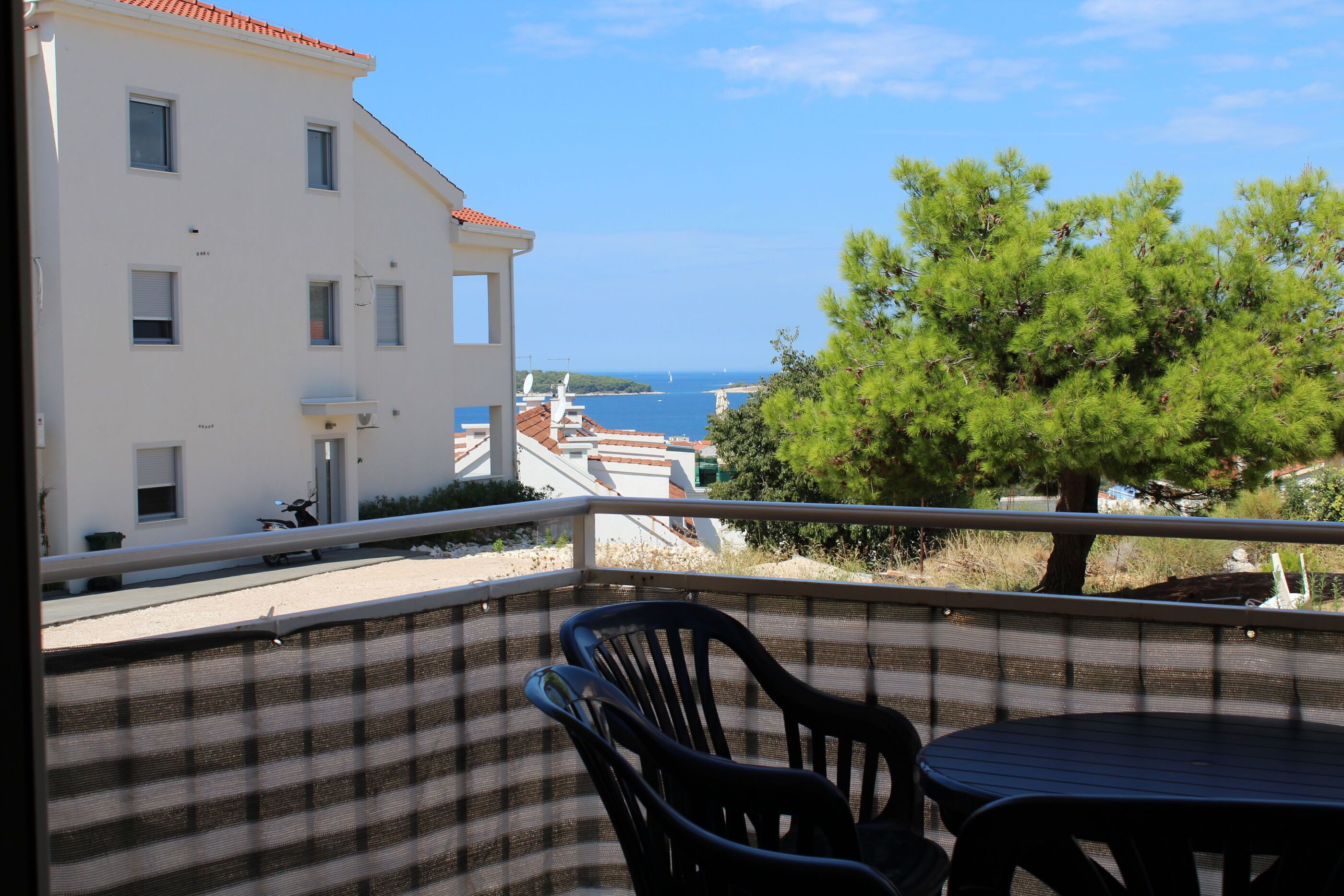 Ein Balkon mit Blick auf das Meer, ein Gebäude und ein Baum.