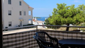 A balcony with a view of the sea, a building, and a tree. - Apartment Mario (Rogoznica)