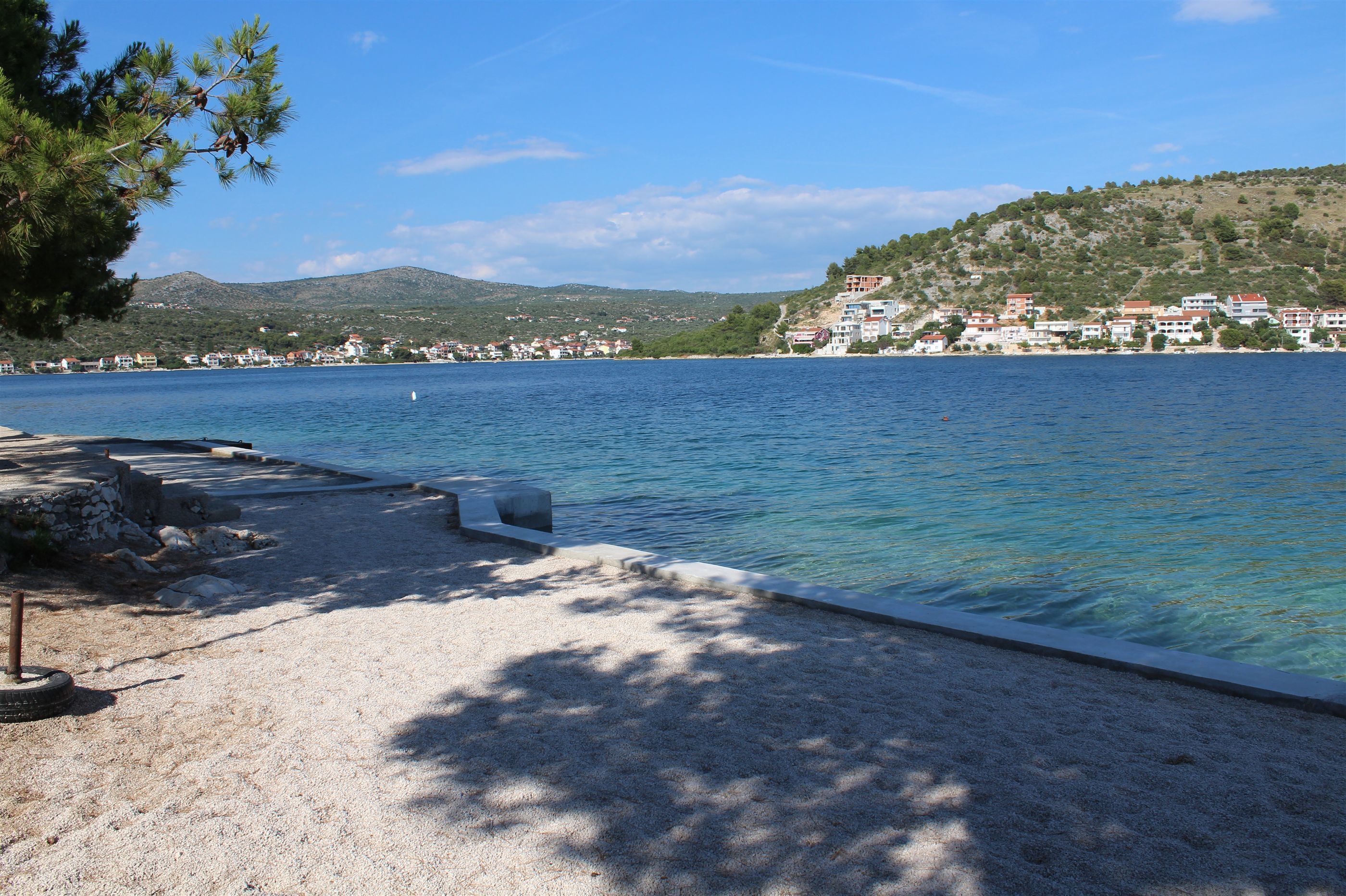A coastal area with a sandy beach, a pier, and buildings on a hillside.