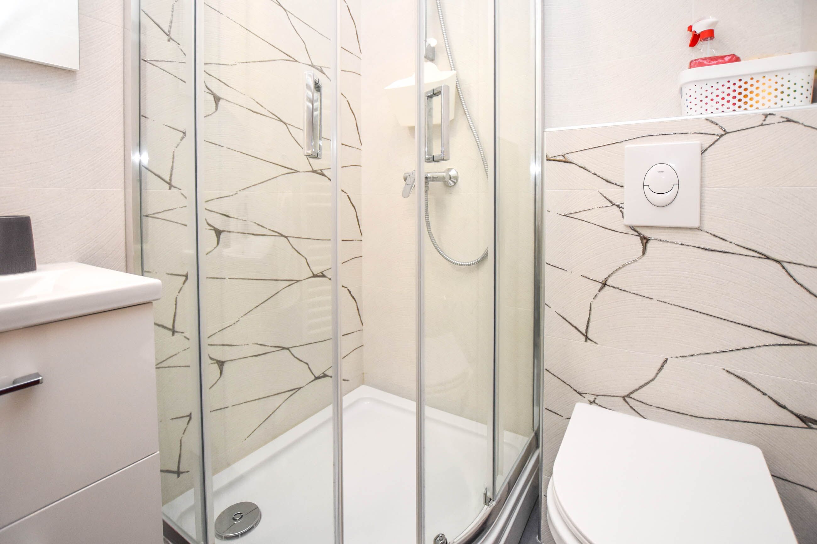 Een badkamer met een douche met glazen wand, een wit toilet en een muur met een patroon van scheuren.