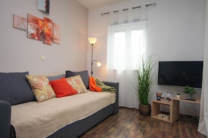 Un salon moderne avec un canapé, une lampe sur pied, un téléviseur et une plante en pot.