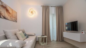 A modern living room with a sofa, a TV on a white cabinet, a painting on the wall, and a window with curtains.