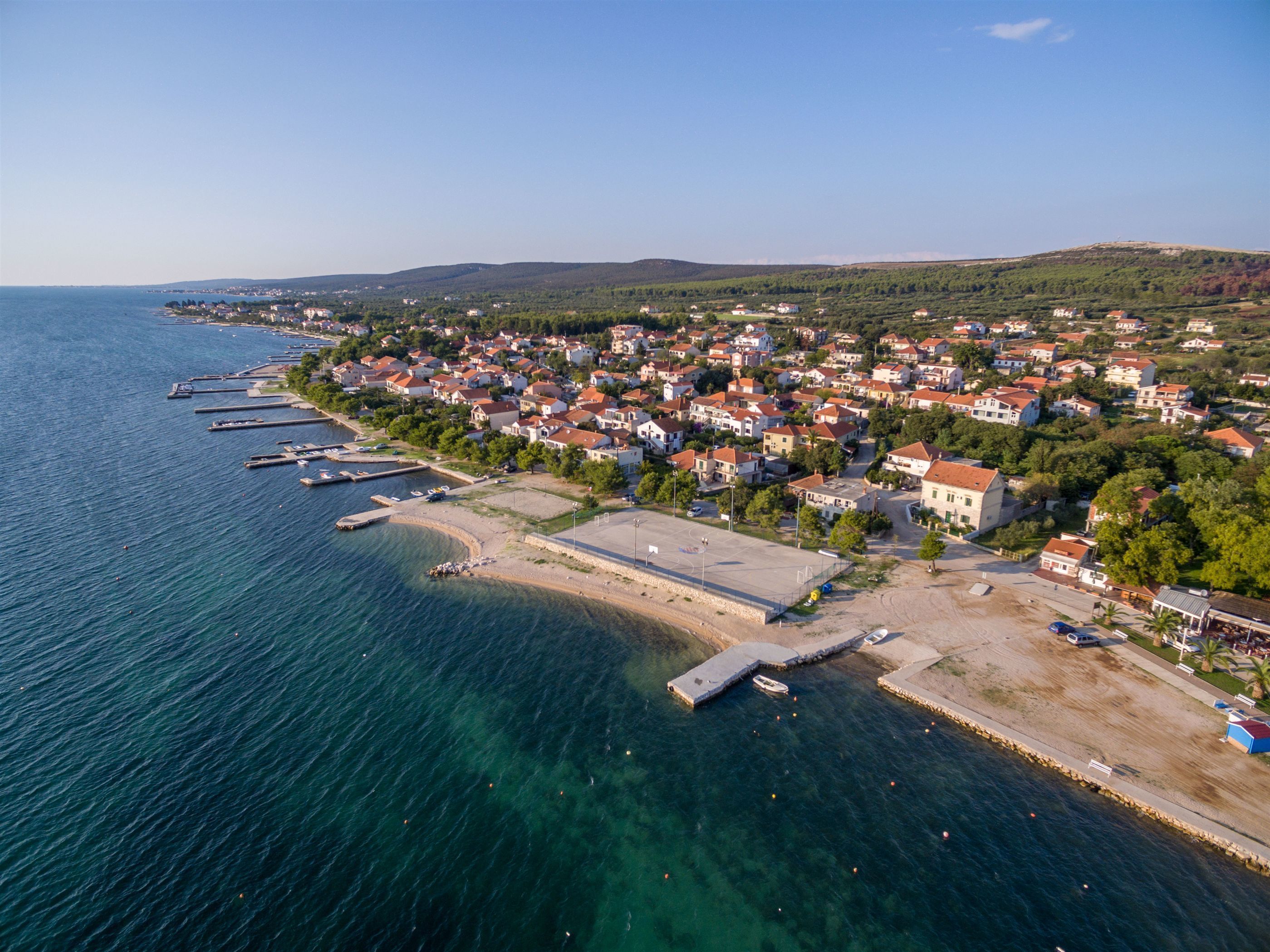 Luftaufnahme einer Küstenstadt mit einer Marina, Wohnhäusern und einem klaren, blauen Meer.
