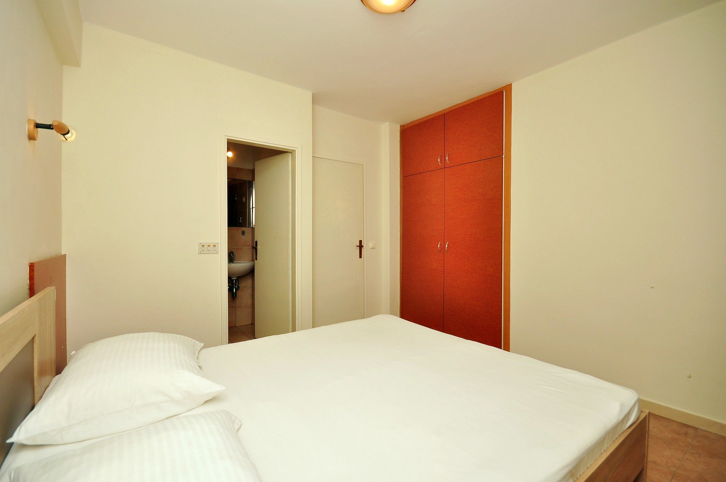 Een slaapkamer met een bed, een kledingkast en een zichtbare badkamer door een open deur.