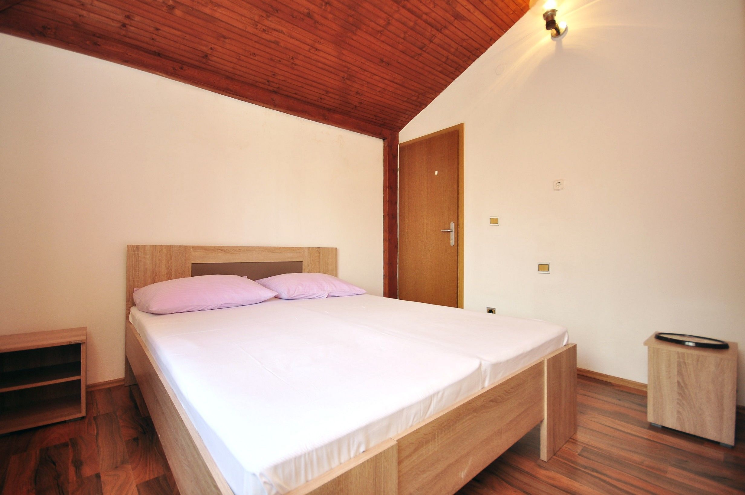 A single bed with a wooden headboard in a room with wooden flooring and a sloped ceiling.