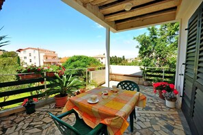 Une terrasse extérieure couverte, avec une table dressée pour deux, entourée de plantes en pot et offrant une vue sur le quartier.