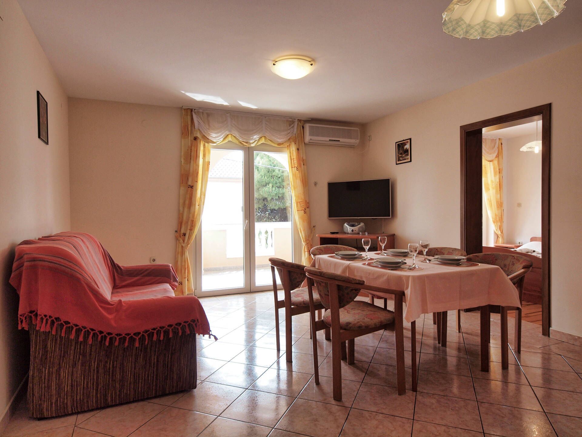 A dining area with a table set for four, a sofa, and a television on the wall.