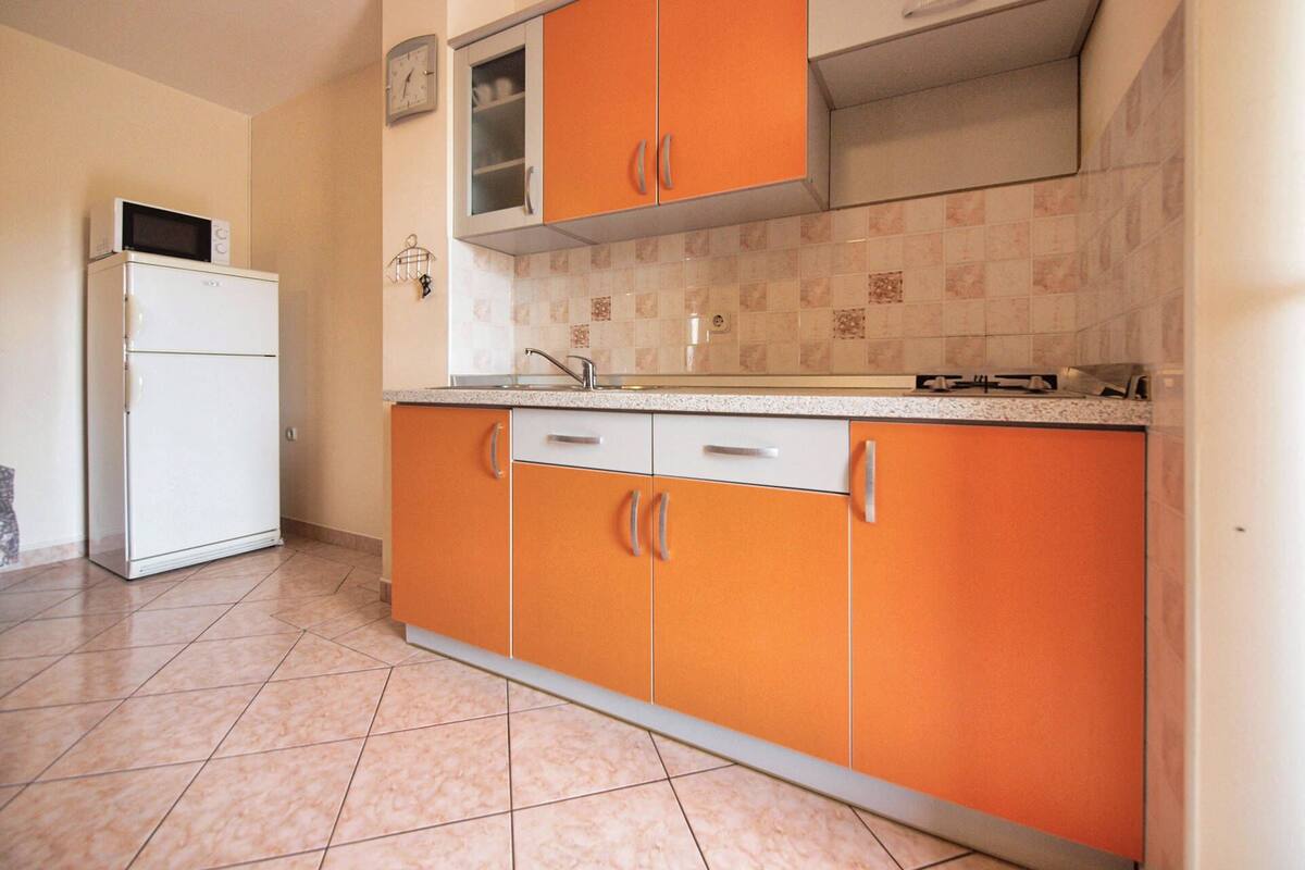 A kitchen with orange cabinets, a white refrigerator, and a tiled backsplash.