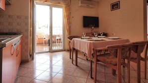 A dining area with a table set for four, a kitchen with a stove, and a sliding glass door leading to an outdoor patio. - Apartments Vladimir (Vodice)