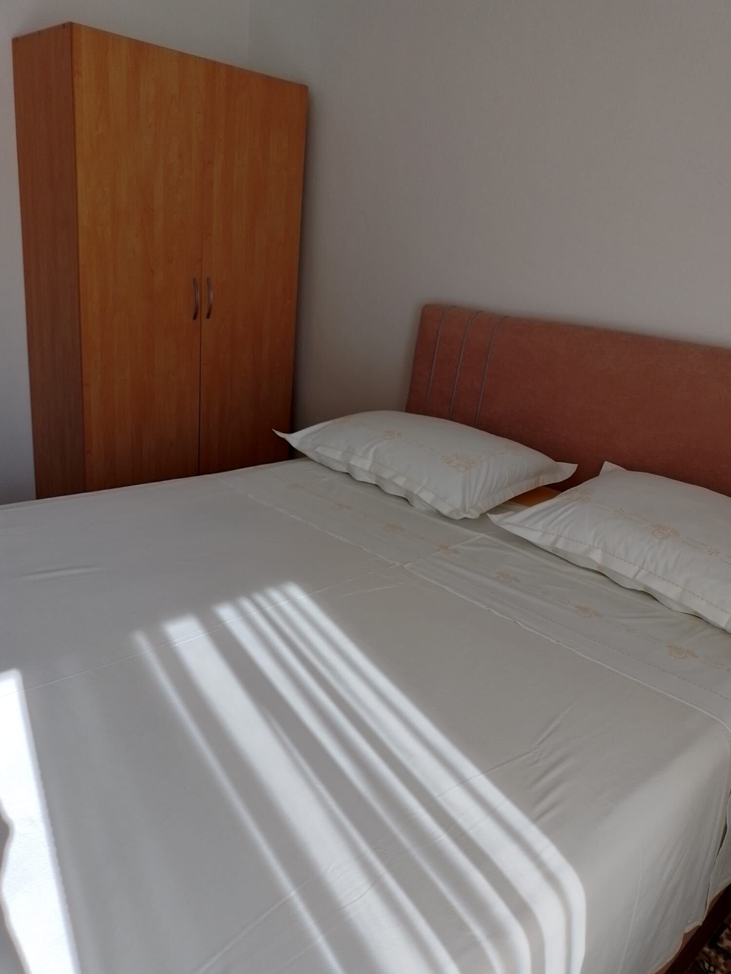 A bedroom with a bed, white bedding, a wooden wardrobe, and a headboard.