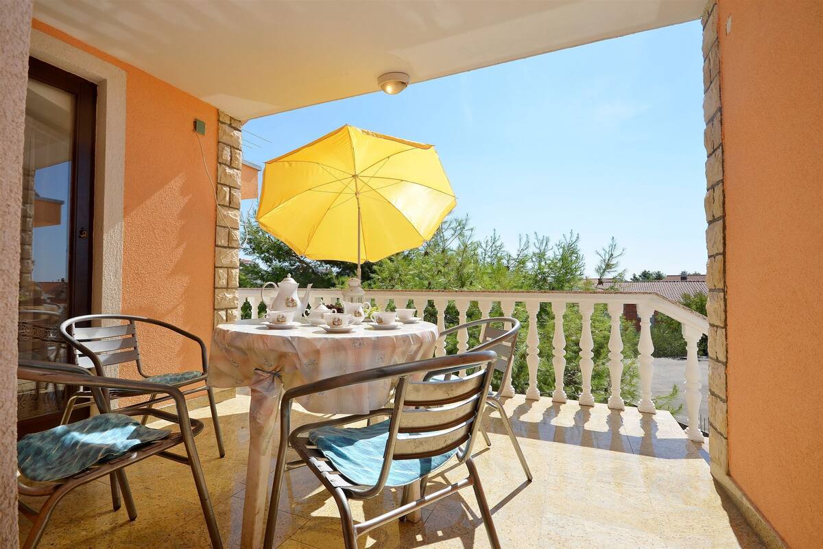 A balcony with a table set for tea, a yellow umbrella, and chairs.