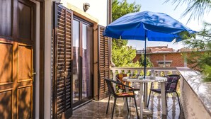 A balcony with a table and chairs, a blue umbrella, and a view of a brick building. - Apartments Miljenka (Vodice)