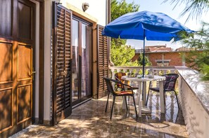 A balcony with a table and chairs, a blue umbrella, and a view of a brick building.