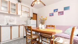 A compact kitchen with wooden cabinets, a dining table with chairs, and a sofa in the adjacent living area. - Apartments Miljenka (Vodice)