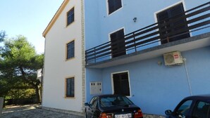 A two-story building with a balcony on the upper floor, a car parked in front, and an air conditioning unit on the wall. - Apartments Miljenka (Vodice)