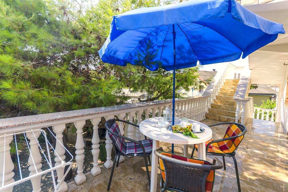 A balcony with a round table, two chairs, a blue umbrella, and a stone staircase.