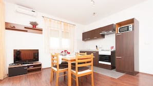 A modern kitchen with wooden cabinets, a microwave, and a dining area with a TV and wooden chairs. - Apartments Tatjana (Sukosan)