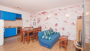 A compact living space with a kitchenette, a dining area, and a seating area with a sofa and a TV. - Apartments Tatjana (Sukosan)