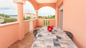 A balcony with a table and chairs, a vase of flowers, and a view of the sea and buildings. - Apartments Tatjana (Sukosan)