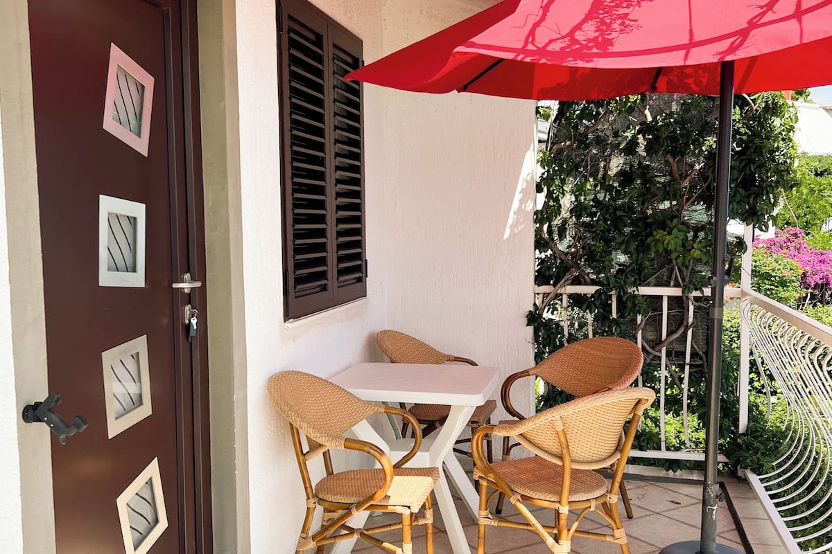 Une terrasse avec une table et des chaises, un parasol rouge et une porte ornée de panneaux de verre décoratifs.