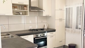 A modern kitchen with white cabinetry, a stainless steel stove, and a built-in oven. There is a trash bin and a potted plant on the counter. - Apartments Vedran (Stanici)