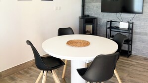 A modern dining area with a round table, black chairs, a white cabinet, and a flat-screen TV mounted on a brick wall. - Apartments Vedran (Stanici)