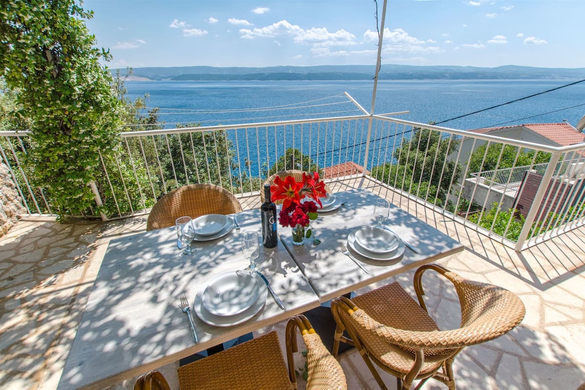Une terrasse avec une table dressée pour deux personnes, donnant sur un plan d’eau.