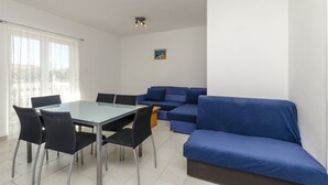 Un salon moderne avec une table à manger en verre, des chaises noires, un canapé bleu et une petite table d’appoint en bois.