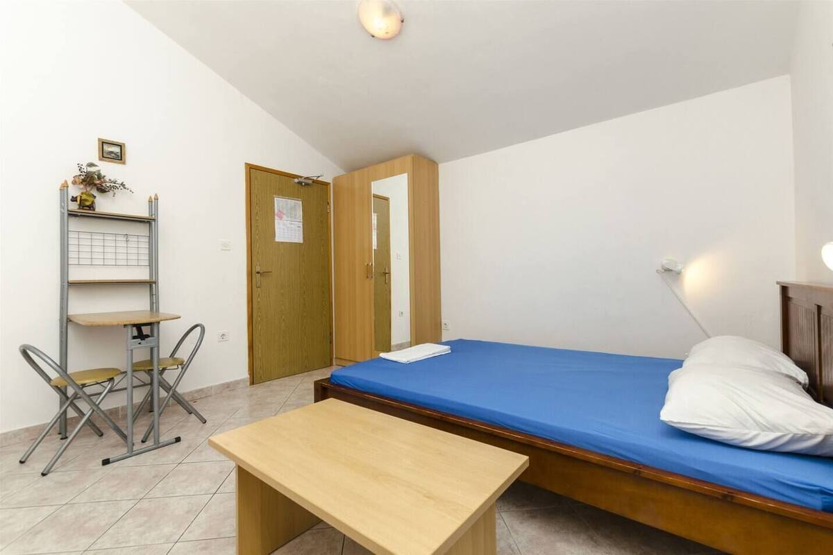 A small, simple room with a bed, a desk, and a chair.