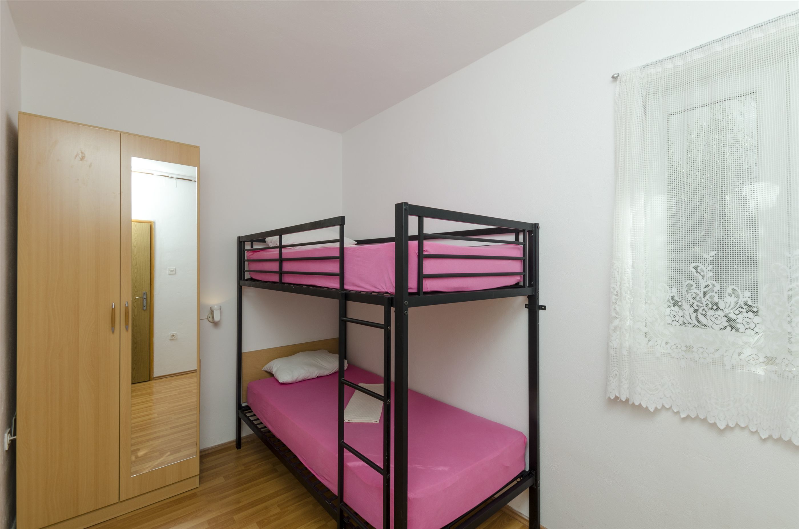 A bunk bed room with a wooden wardrobe and a lace curtain.