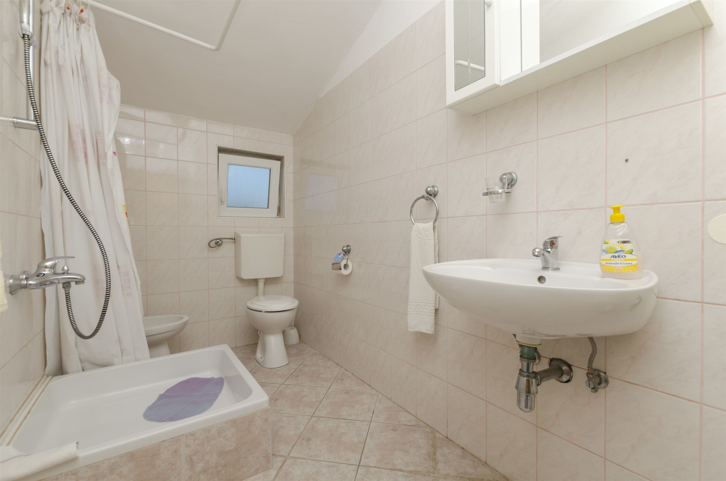 A bathroom with a bathtub, toilet, sink, and a window above the toilet.