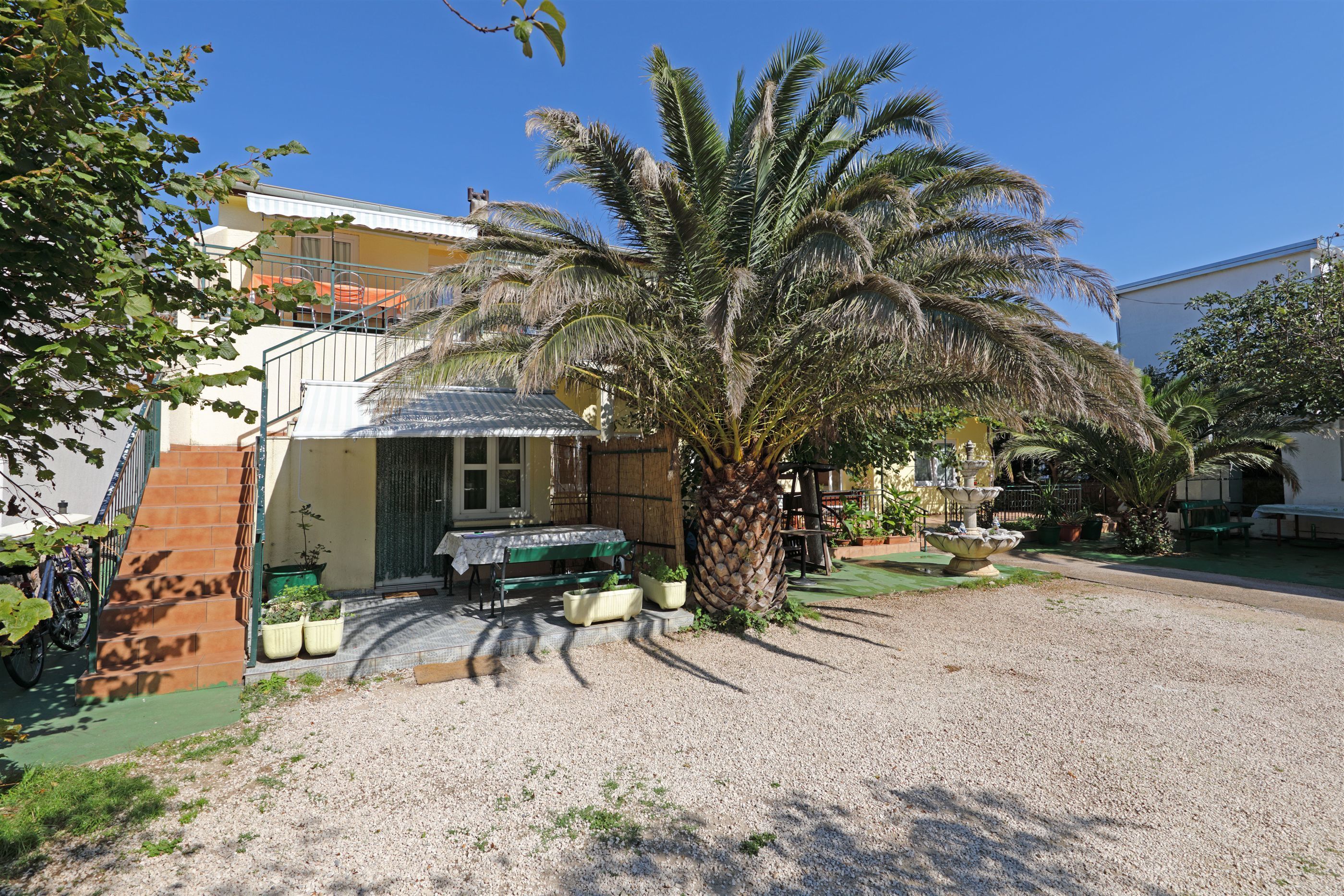 Zona residencial con una palmera, una bicicleta y un pequeño patio con mesa y sillas.
