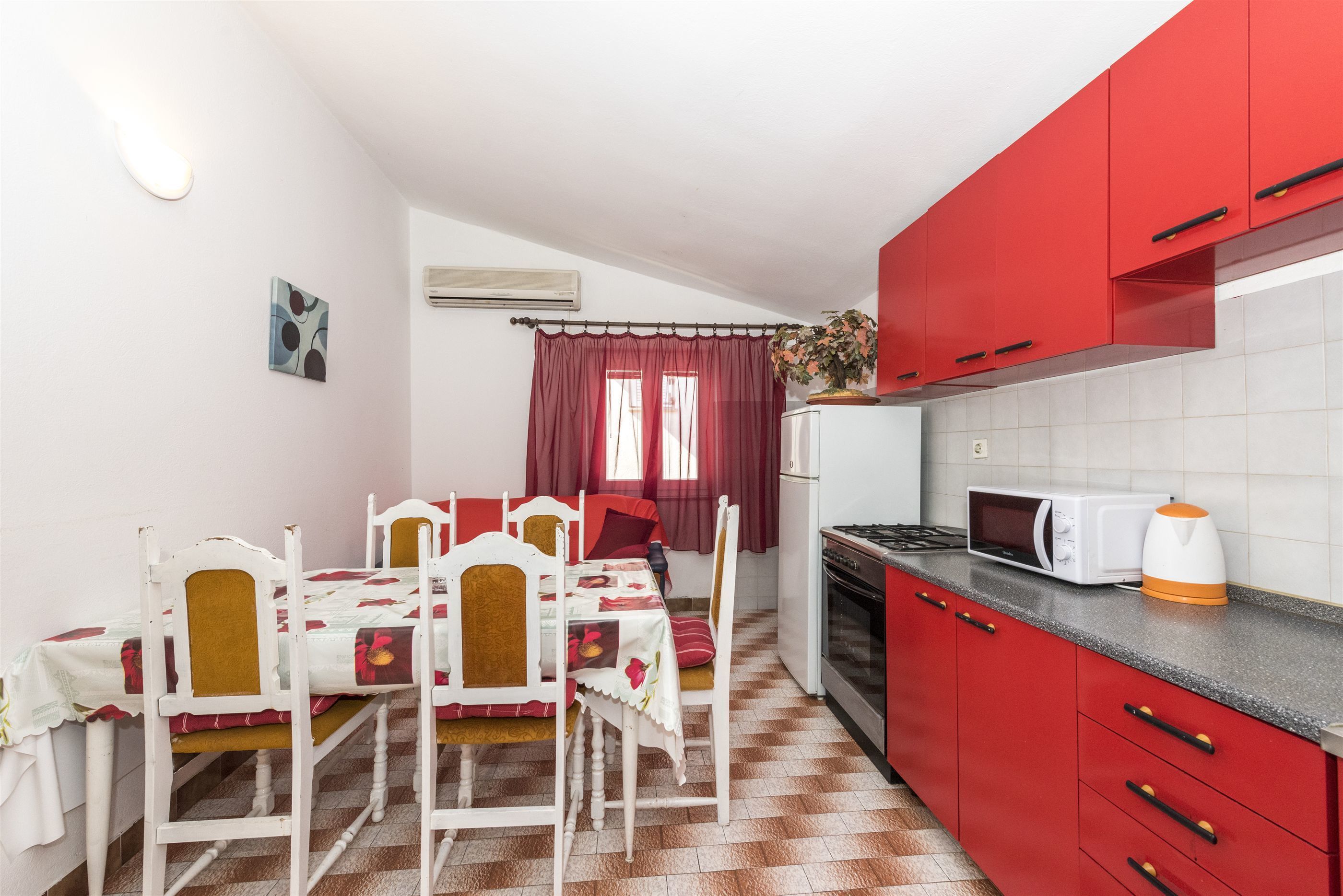 A compact kitchen with red cabinets, a microwave, and a kettle on the counter.