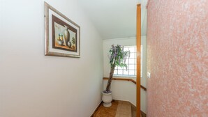 Um corredor com um quadro emoldurado, um vaso de planta e uma janela com luz natural.