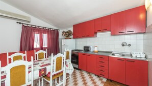 Cozinha compacta com armários vermelhos, micro-ondas e fogão. Há uma mesa de jantar com cadeiras e uma janela com cortinas vermelhas.