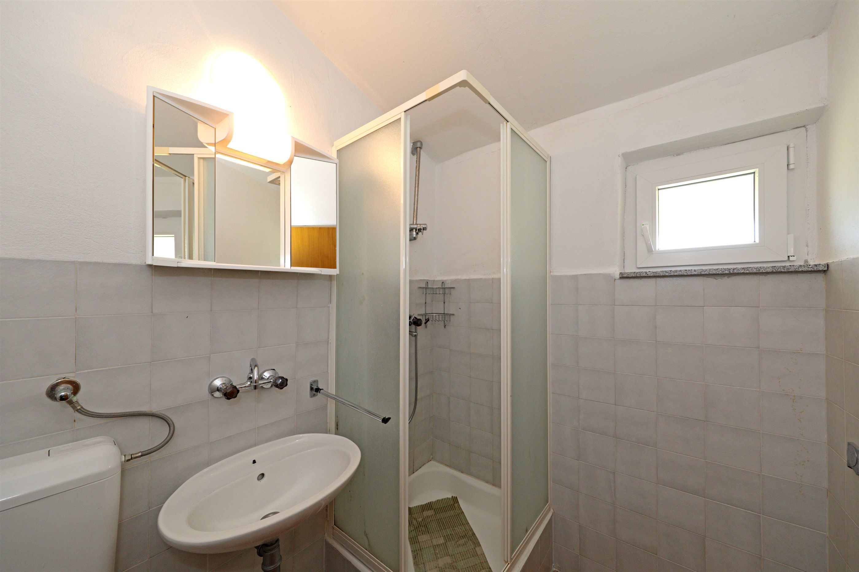 Un baño con lavamanos, espejo, ducha y ventana.