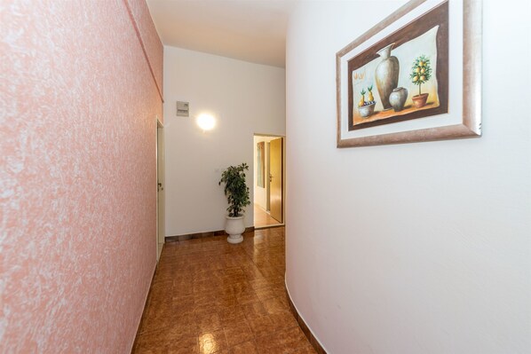 Un pasillo con pared rosa con textura, una planta en maceta y un cuadro en la pared.