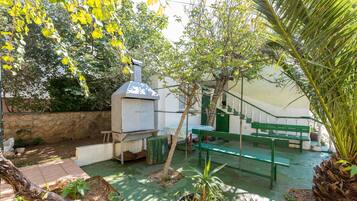 A patio area with a barbecue grill, green benches, potted plants, and a stone wall.