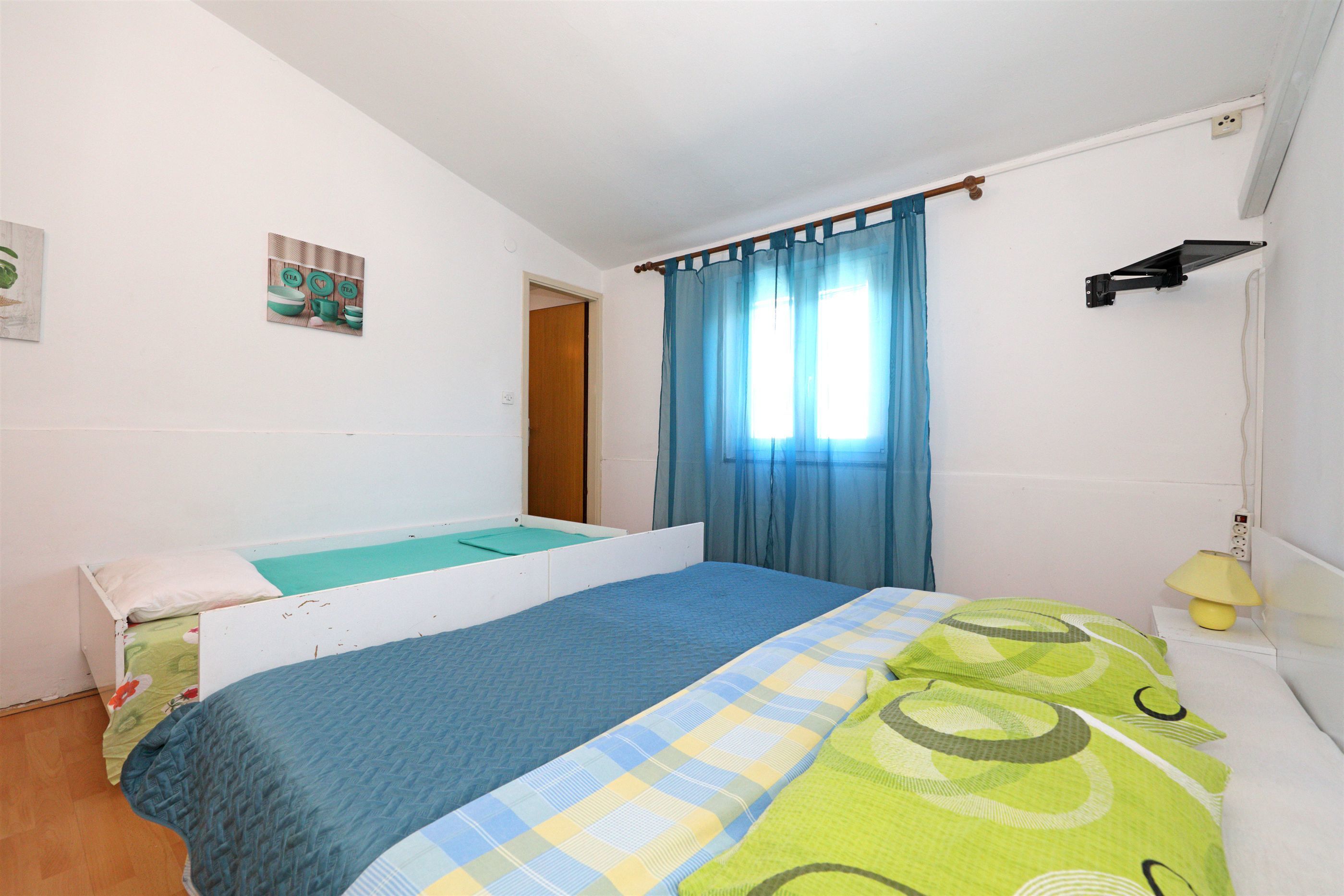 A bedroom with a bed, a bedside table, a lamp, and a window with curtains.