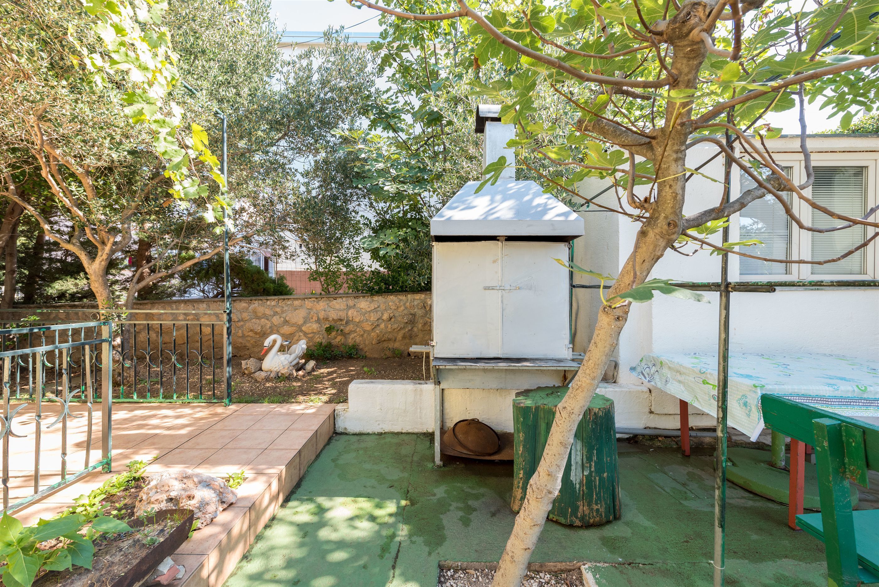 A patio area with a barbecue grill, a table with a tablecloth, and a swan statue.