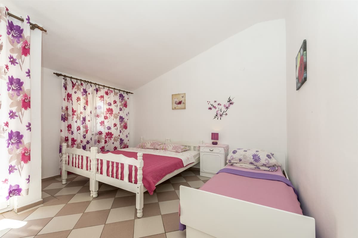A bedroom with two beds, a nightstand, a dresser, and a window with floral curtains.