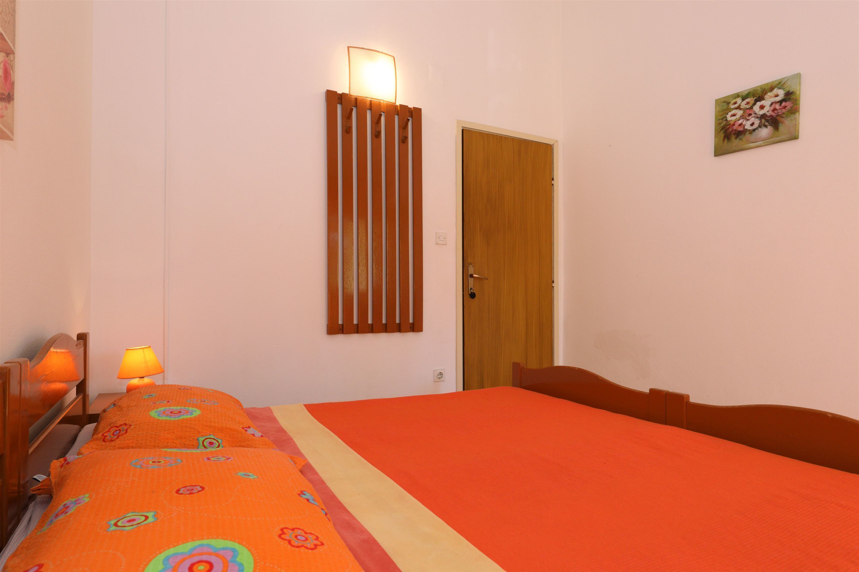 A bedroom with a bed, bedside lamps, a wooden door, and a wall-mounted light fixture.