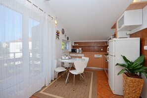 A compact kitchen with white appliances, a dining table with chairs, and a potted plant.