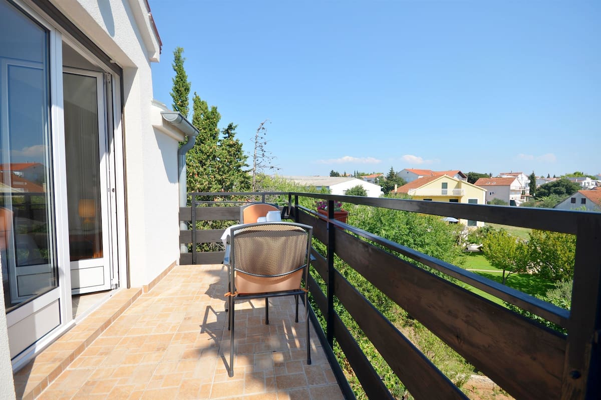 Ein Balkon mit Stuhl und Tisch, der auf einen Wohnbereich mit Häusern und Grünflächen blickt.