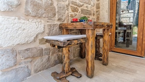 Un banco de madera rústica con un asiento acolchado y una pequeña mesa con una planta y una taza roja.