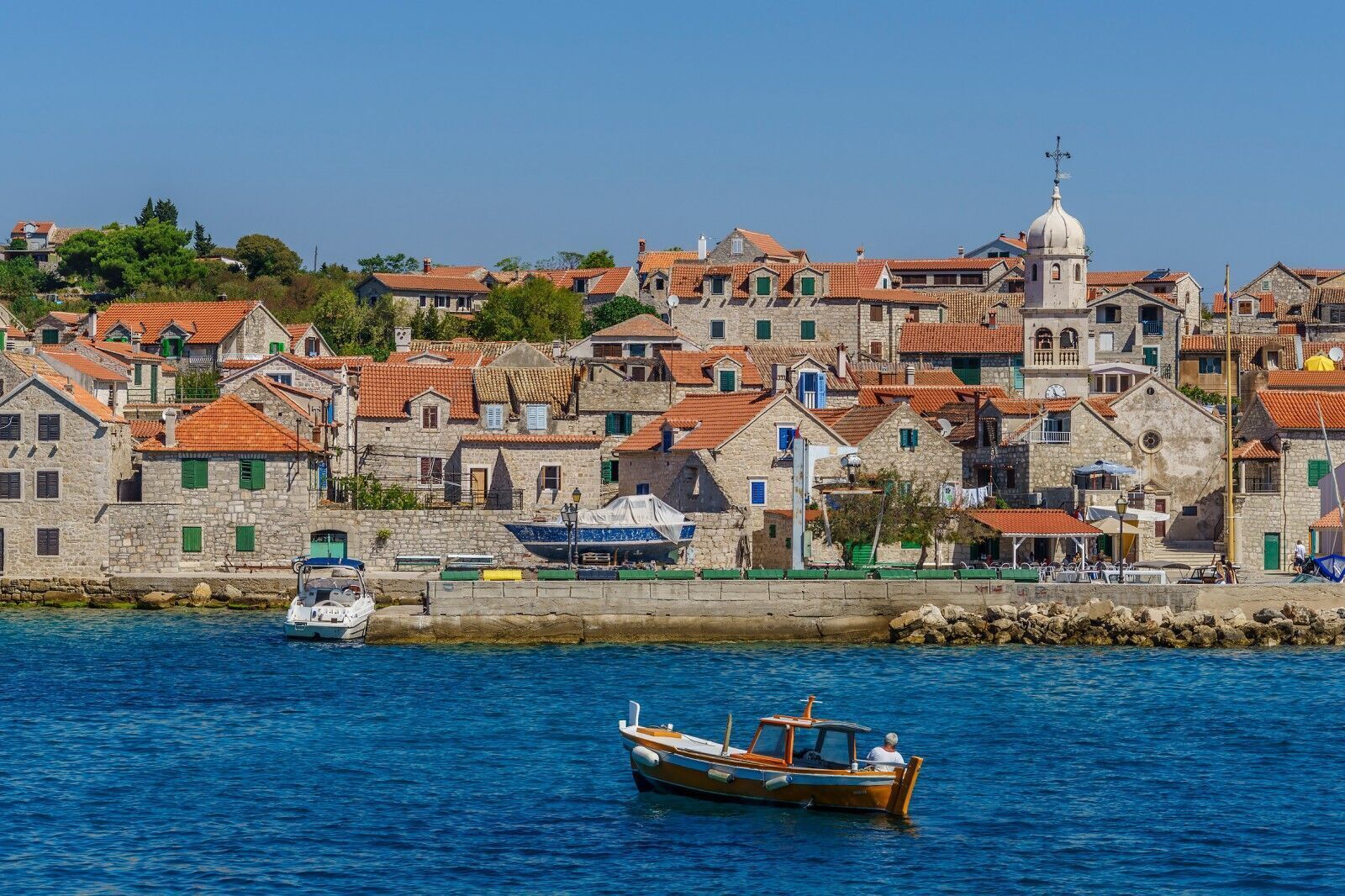 A coastal town with stone buildings, a church with a dome, and a boat in the water.