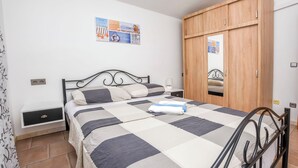 Une chambre à coucher comprenant un lit, une table de chevet, une armoire en bois et un mur orné d’un tableau encadré.